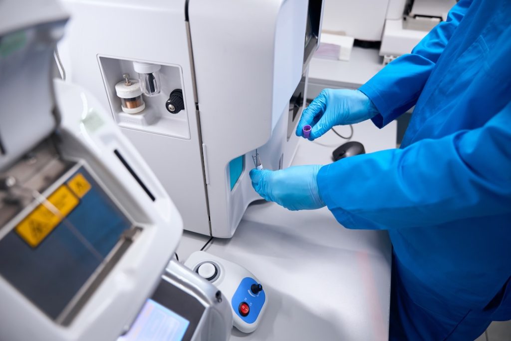 Man in a uniform works on an apparatus for automatic isolation of nucleic acids, a man wearing protective gloves